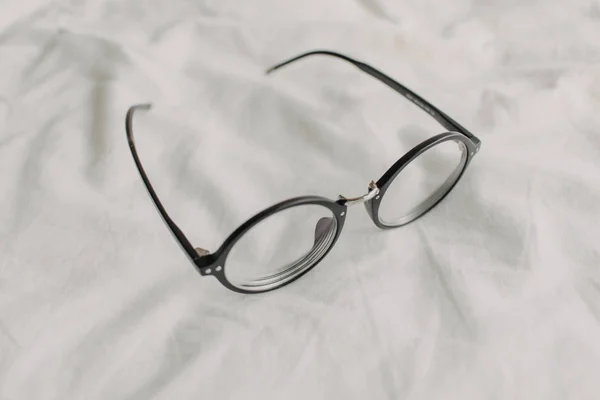 Brille mit schwarzem Kunststoffbügel auf weißem Bettlaken. — Stockfoto