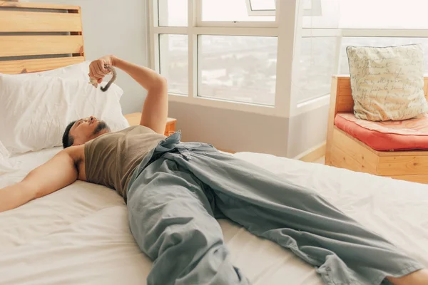 Asiático homem deitar na cama e relaxar em seu apartamento no calor domingo verão primavera . — Fotografia de Stock