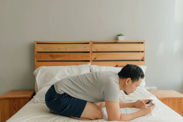 Homem está jogando jogo móvel com seu smartphone na cama . — Fotografia de Stock