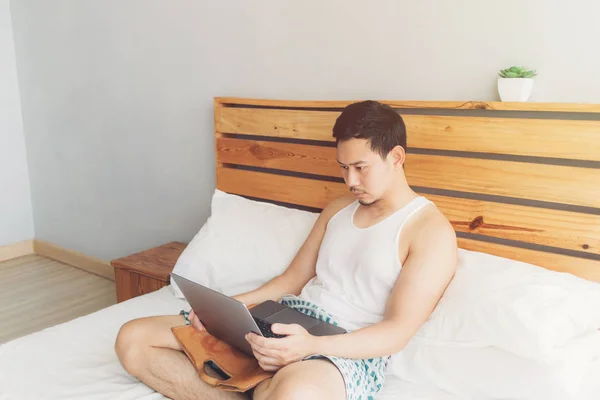 Lonely man is working with his laptop on his cozy bed. Concept of freelancer work lifestyle.