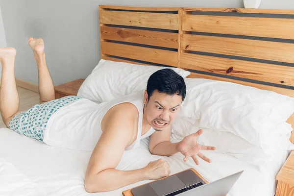 El hombre enojado está trabajando con su portátil en su cama. Concepto de problemas de freelancer . — Foto de Stock