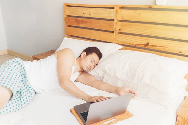 Сонный человек работает со своим ноутбуком на своей уютной кровати. Концепция скучного фрилансерского образа жизни . — стоковое фото