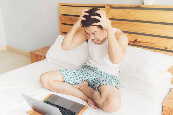 O homem zangado está a trabalhar com o portátil na cama. Conceito de problemas freelancer . — Fotografia de Stock