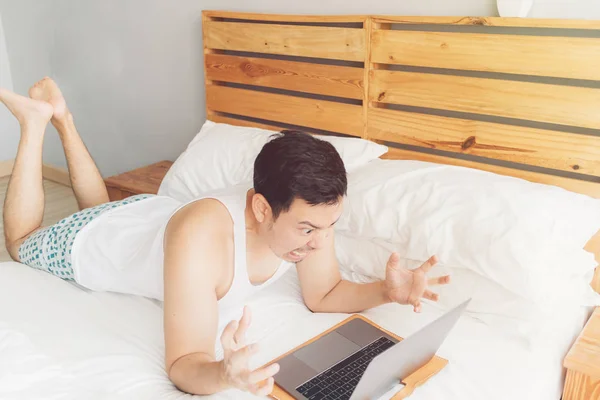 Злой человек работает со своим ноутбуком на кровати. Концепция проблем фрилансеров . — стоковое фото