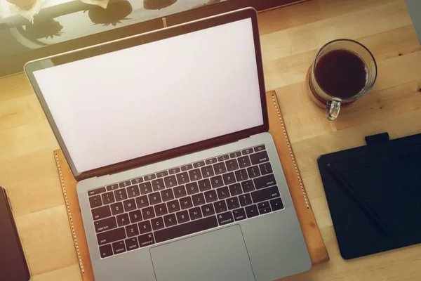 Freelance workspace laptop on wooden desk with window light.