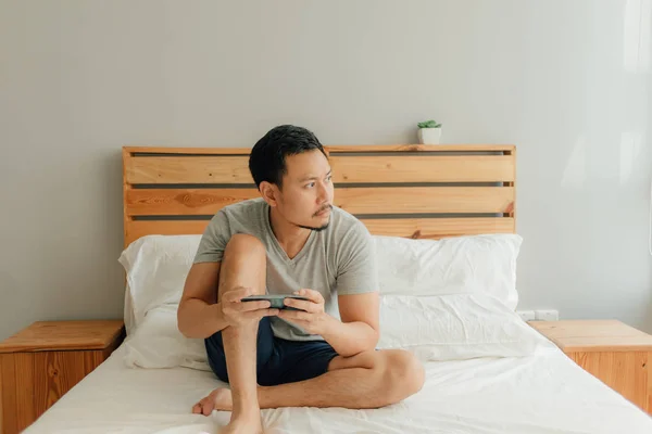 Homem está jogando jogo móvel com seu smartphone na cama . — Fotografia de Stock