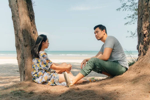 Par sitter tillsammans i på stranden under trädet tall. — Stockfoto