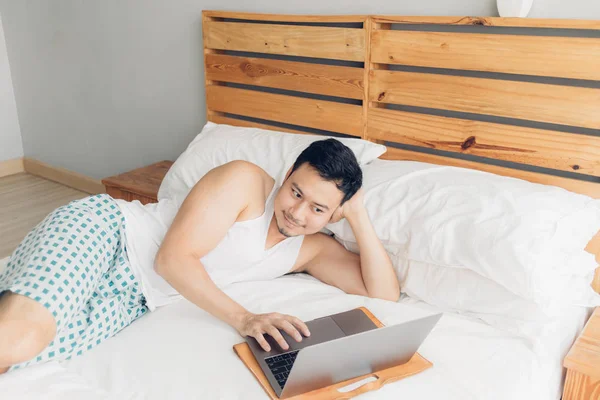 행복한 남자는 자신의 침대에 자신의 노트북으로 작업하고 있습니다. 프리랜서 성공적인 라이프 스타일의 개념. — 스톡 사진