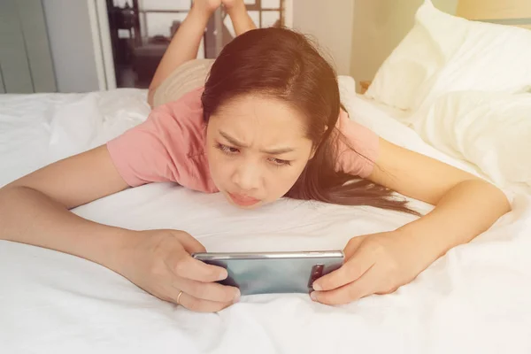 Mulher perturbada está jogando jogo móvel em sua cama . — Fotografia de Stock