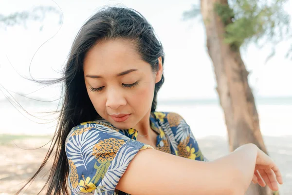 Kvinnan kollar sin klänning när man går på stranden med träd tall. — Stockfoto