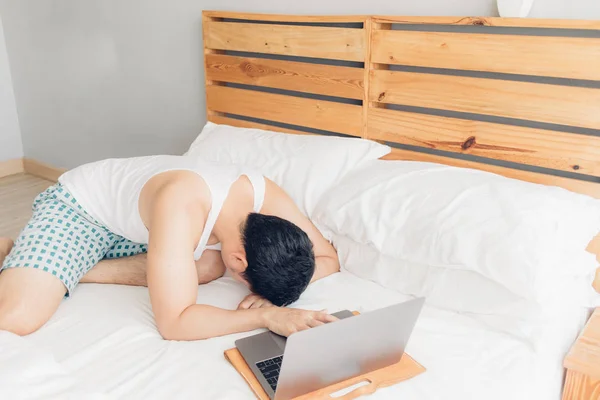 Sleepy hombre está trabajando con su portátil en su acogedora cama. Concepto de aburrido estilo de vida freelancer . — Foto de Stock