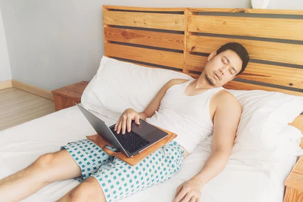 Сонний чоловік працює зі своїм ноутбуком на своєму затишному ліжку. Концепція нудного способу життя фрілансера . — стокове фото
