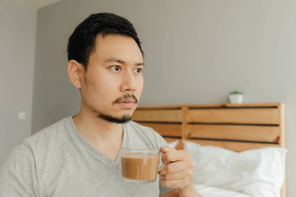 Seorang pria minum secangkir kopi di tempat tidur di kamar tidurnya . — Stok Foto