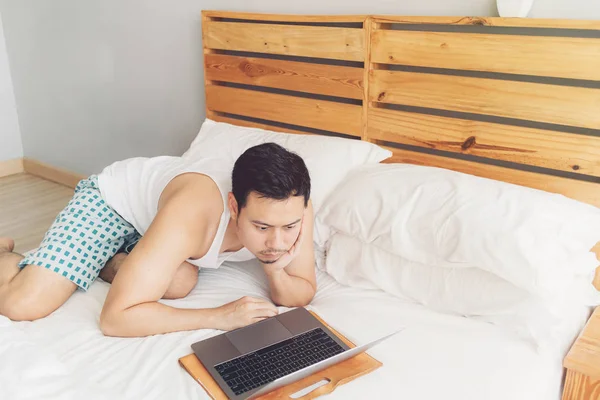 Pria kesepian bekerja dengan laptopnya di tempat tidurnya yang nyaman. Konsep gaya hidup pekerja lepas . — Stok Foto