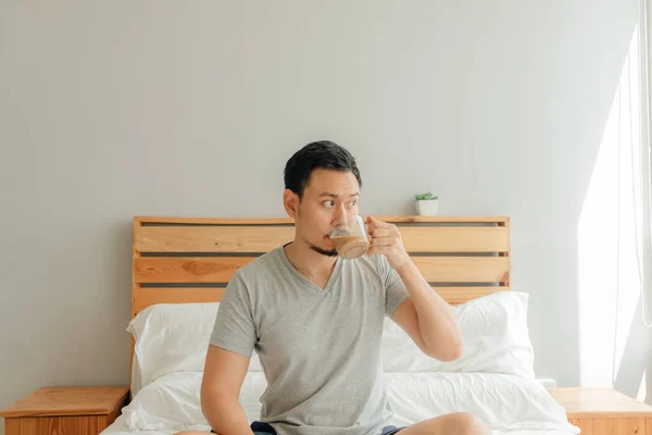 Чоловік п'є чашку кави на ліжку у своїй спальні . — стокове фото