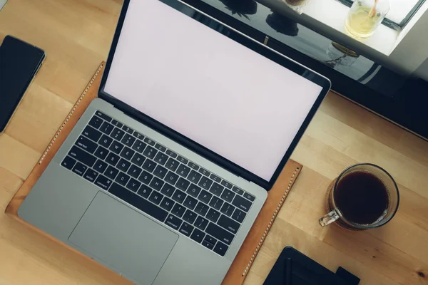 Freelance workspace laptop on wooden desk with window light.