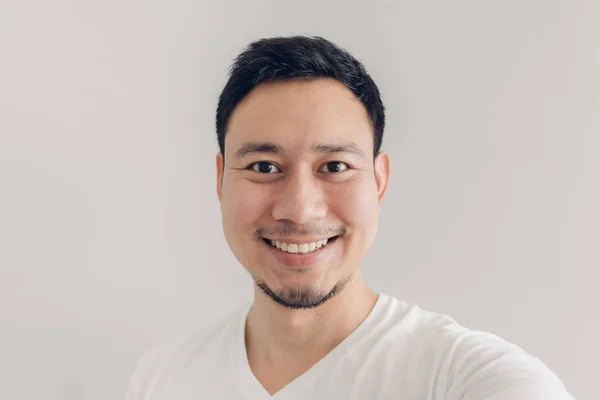 Hymyilevä mies ottaa selfien itsestään valkoisella t-paidalla ja harmaalla taustalla . — kuvapankkivalokuva
