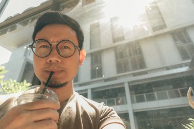 Mutlu adam kafede buzlu kahve içiyor. Parlak güneşten saklanıyor..