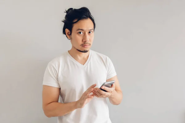 Uomo capelli lunghi in bianco casual t-shirt sta utilizzando smartphone. — Foto Stock