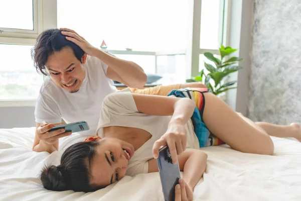 Casal animado está jogando telefone celular juntos em seu apartamento . — Fotografia de Stock