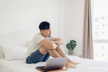 Adam yatakta oturuyor ve dizüstü bilgisayarıyla uğraşıyor..