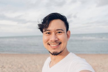 Kumsalda yürürken mutlu selfie çeken adam..