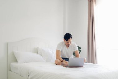 Adam yatakta oturuyor ve dizüstü bilgisayarıyla uğraşıyor..