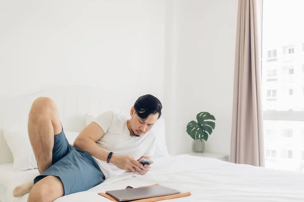 Человек использует смартфон на своей кровати в концепции релаксации. — стоковое фото