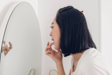 Kadın beyaz odadaki aynada dudaklarını kontrol ediyor..