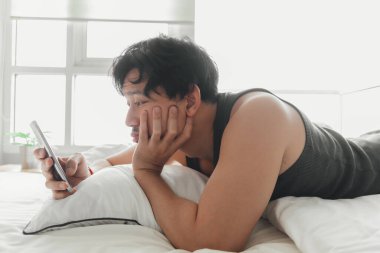 Uykulu adam yatakta yatarken akıllı telefon kullanıyor..