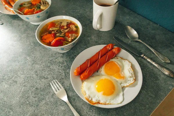 Ontbijt set van gebakken eierworstjes en groentesoep geserveerd op tafel. — Stockfoto