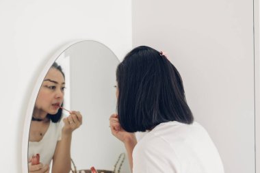 Kadın beyaz odadaki aynada dudaklarını kontrol ediyor..