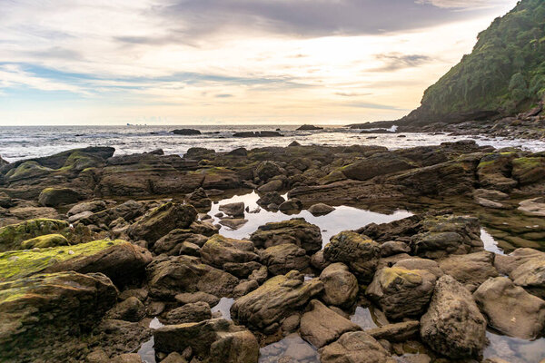 Beach rocks with sunset and calm cloudy sky.