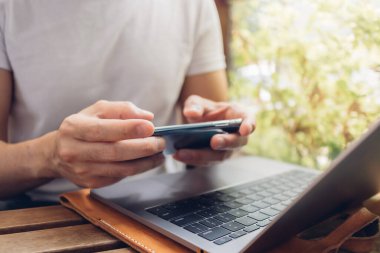 Beyaz tişörtlü adam kafeteryada akıllı telefon ve laptop kullanıyor..