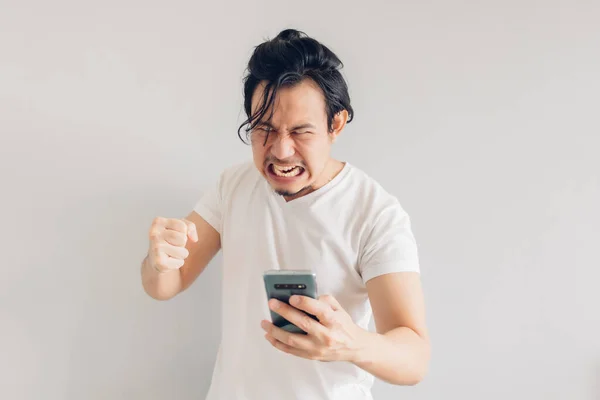 Dühös és dühös hosszú hajú férfi fehér pólóban okostelefont használ. — Stock Fotó
