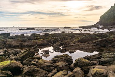 Gün batımlı plaj kayaları ve sakin bulutlu gökyüzü.