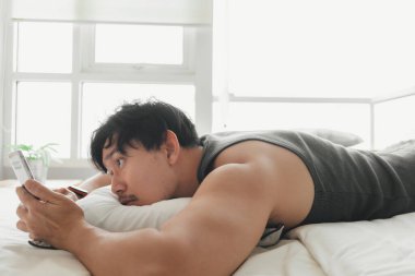 Uykulu adam yatakta yatarken akıllı telefon kullanıyor..