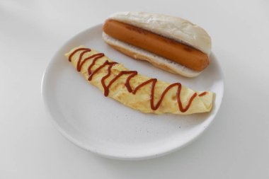 Beyaz masada servis edilen basit bir omlet ve sosis kahvaltısı..