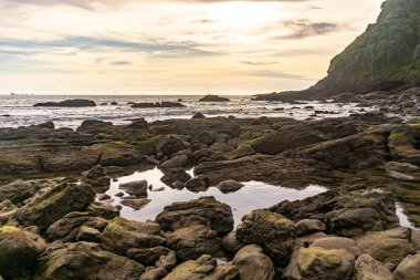 Gün batımlı plaj kayaları ve sakin bulutlu gökyüzü.