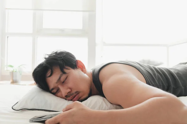 Sleepy hombre está utilizando el teléfono inteligente mientras está acostado en la cama. — Foto de Stock