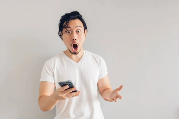 Surpreso e chocado homem de cabelo longo em t-shirt branca está usando smartphone. — Fotografia de Stock