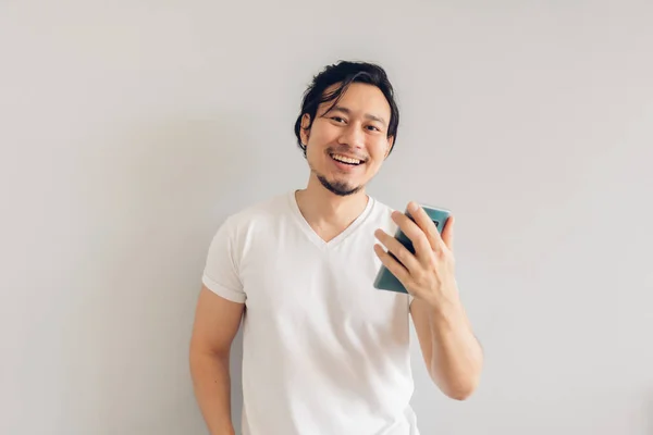 Sorriso e felice uomo capelli lunghi in bianco casual t-shirt sta utilizzando smartphone. — Foto Stock