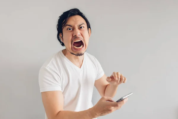 Dühös és dühös hosszú hajú férfi fehér pólóban okostelefont használ. — Stock Fotó
