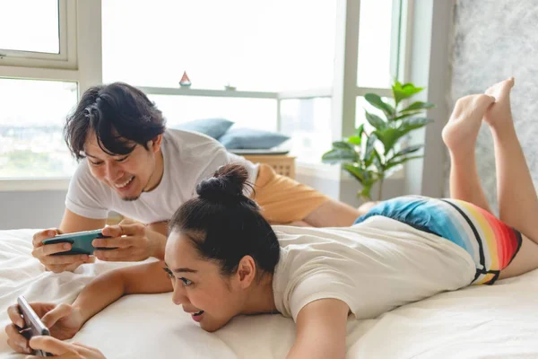 Casal feliz está jogando jogo móvel juntos em sua cama. — Fotografia de Stock