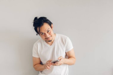 Gülümse ve mutlu uzun saçlı beyaz tişörtlü adam akıllı telefon kullanıyor..