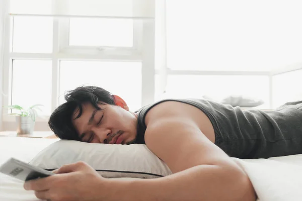 Sleepy man is using smartphone while lying on the bed. — Stock Photo, Image