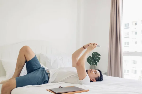 Homem está usando o smartphone em sua cama em conceito de relaxamento. — Fotografia de Stock
