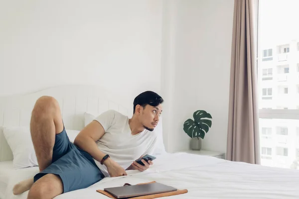 Homem está usando o smartphone em sua cama em conceito de relaxamento. — Fotografia de Stock