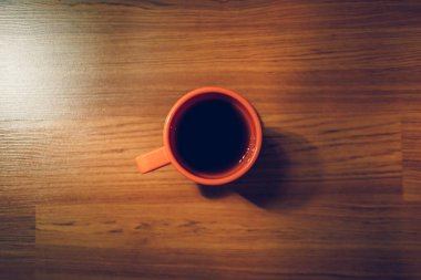 Alçak ışıkta, ahşap zeminde portakallı sıcak kahve kupası..