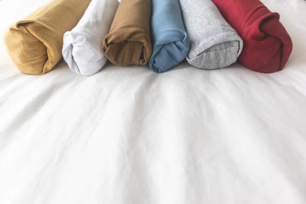 Coloridos rollos de camiseta en la cama blanca. — Foto de Stock
